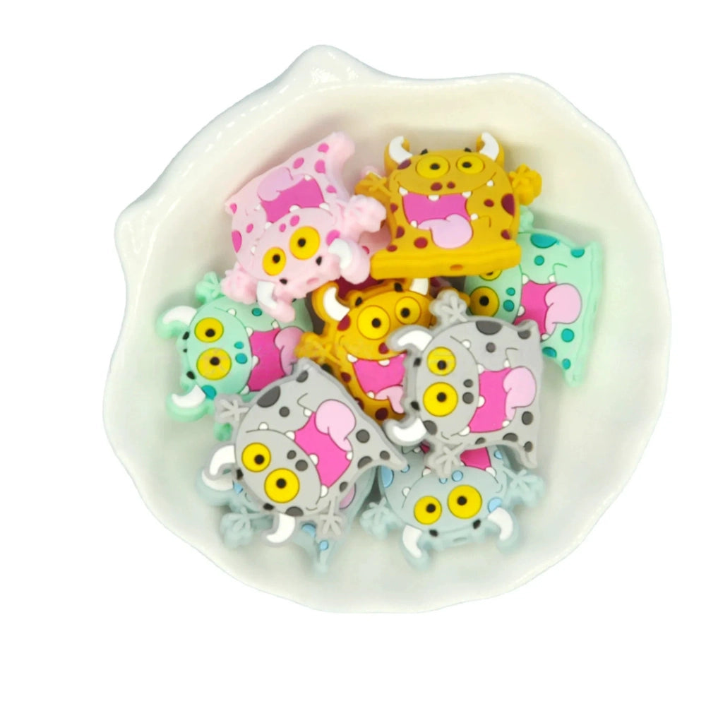Assorted cartoon monster silicone focal beads in pink, yellow, gray, and mint green with big yellow eyes and horns, displayed in a white ceramic dish for DIY crafting projects. - Random Mixed