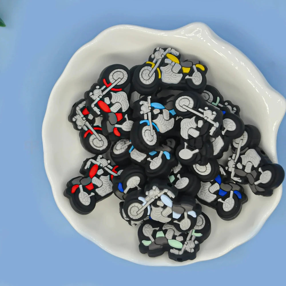 Assorted color motorcycle silicone focal beads in red, blue, yellow, green, and white displayed in a white dish on a blue background, for DIY beadable pens and keychains.