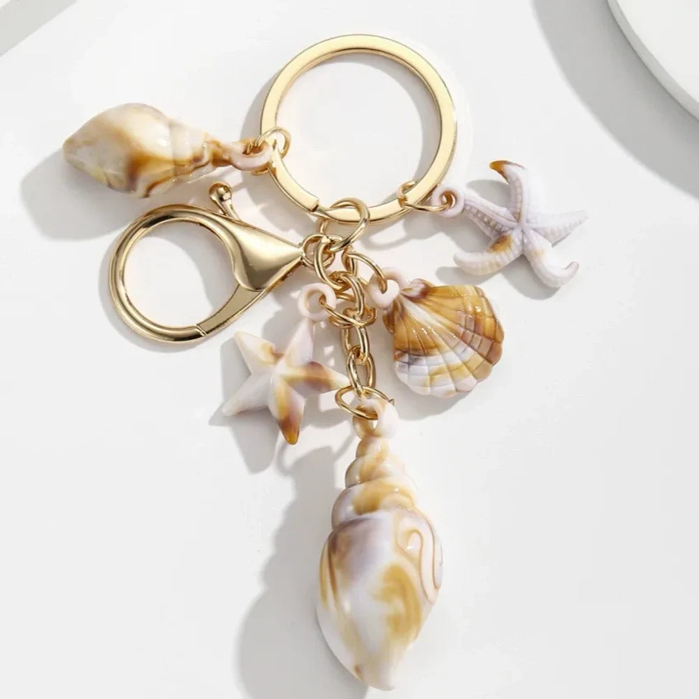 Five natural seashell keychain charms featuring conch shells, starfish, and scallop shells on gold-tone key rings, arranged on a white surface for DIY jewelry making and beach-themed crafts. - 10