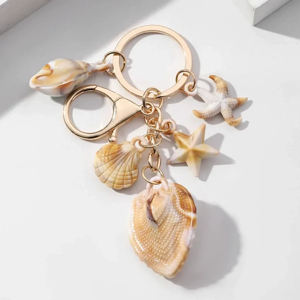 Five natural seashell keychain charms featuring conch shells, starfish, and scallop shells on gold-tone key rings, arranged on a white surface for DIY jewelry making and beach-themed crafts. - 11