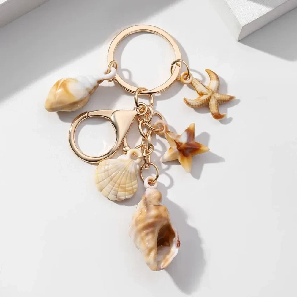 Five natural seashell keychain charms featuring conch shells, starfish, and scallop shells on gold-tone key rings, arranged on a white surface for DIY jewelry making and beach-themed crafts. - 12