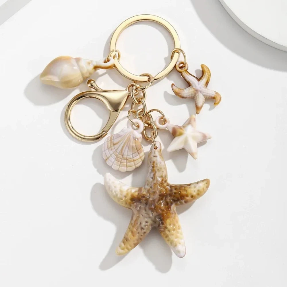 Five natural seashell keychain charms featuring conch shells, starfish, and scallop shells on gold-tone key rings, arranged on a white surface for DIY jewelry making and beach-themed crafts. - 3