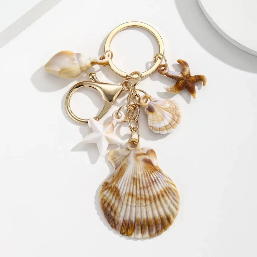 Five natural seashell keychain charms featuring conch shells, starfish, and scallop shells on gold-tone key rings, arranged on a white surface for DIY jewelry making and beach-themed crafts. - 4