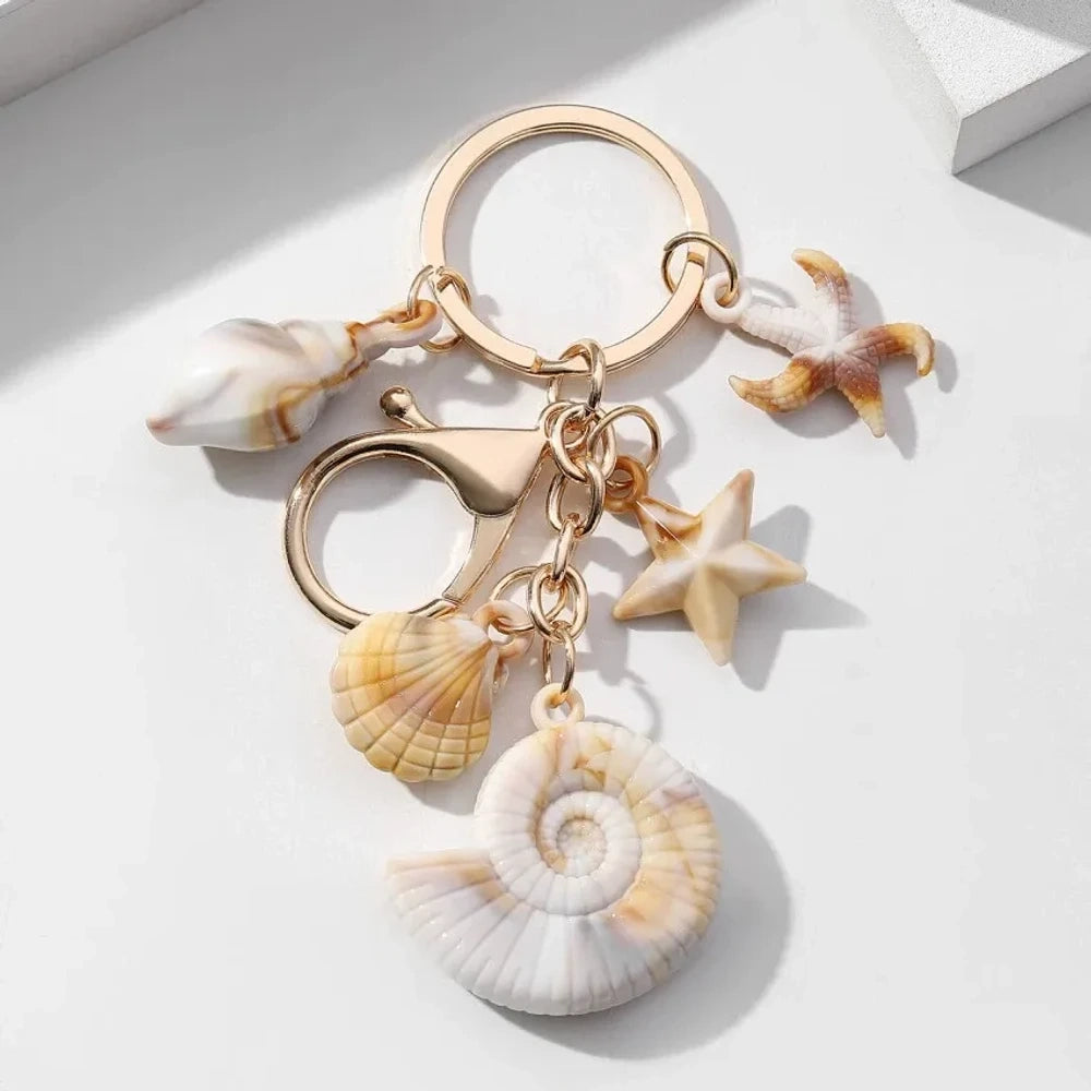 Five natural seashell keychain charms featuring conch shells, starfish, and scallop shells on gold-tone key rings, arranged on a white surface for DIY jewelry making and beach-themed crafts. - 7
