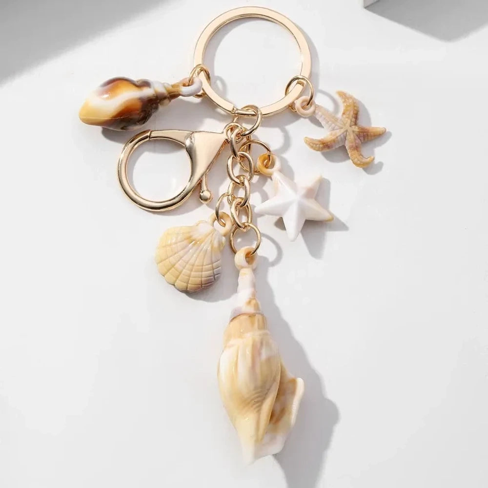 Five natural seashell keychain charms featuring conch shells, starfish, and scallop shells on gold-tone key rings, arranged on a white surface for DIY jewelry making and beach-themed crafts. - 8