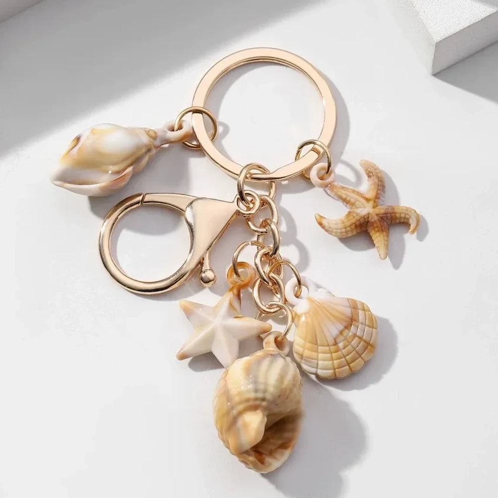 Five natural seashell keychain charms featuring conch shells, starfish, and scallop shells on gold-tone key rings, arranged on a white surface for DIY jewelry making and beach-themed crafts. - 9
