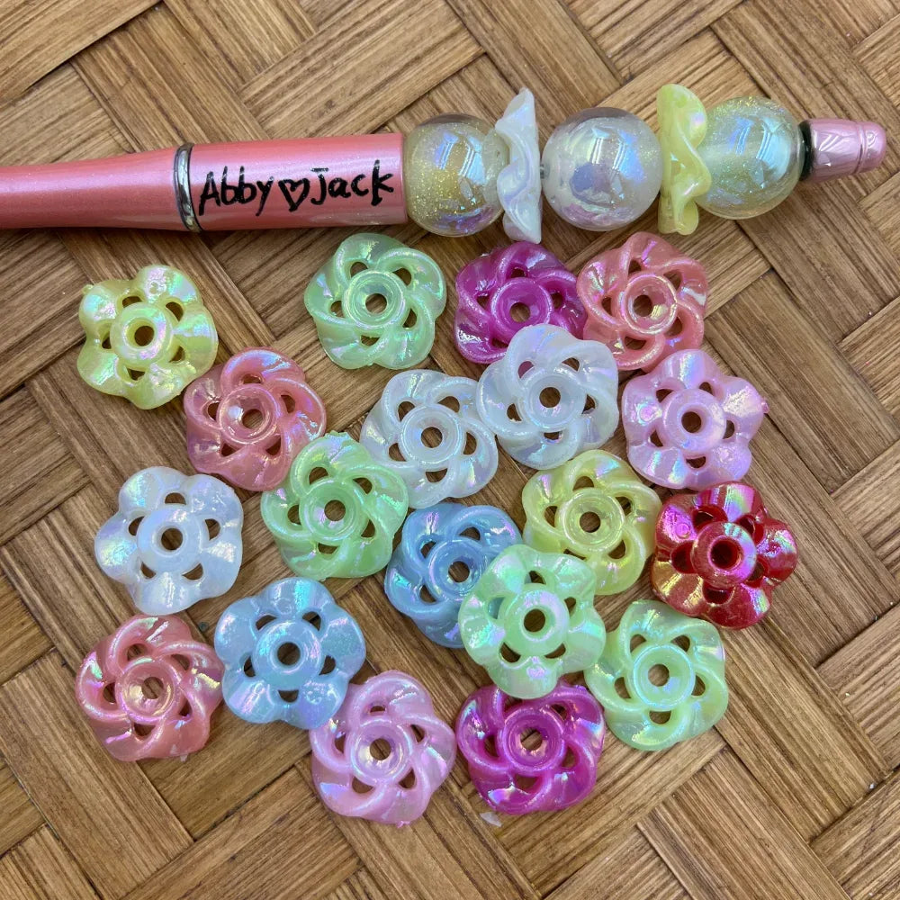 Assorted pastel iridescent open flower acrylic spacer beads beside a pink beadable pen
