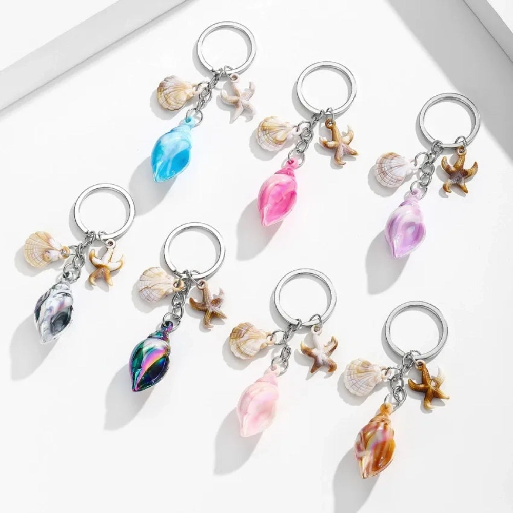 8 colorful ocean-themed resin conch shell charm keychains with starfish and scallop shell pendants on silver rings in blue, pink, purple, rainbow, and brown tones.