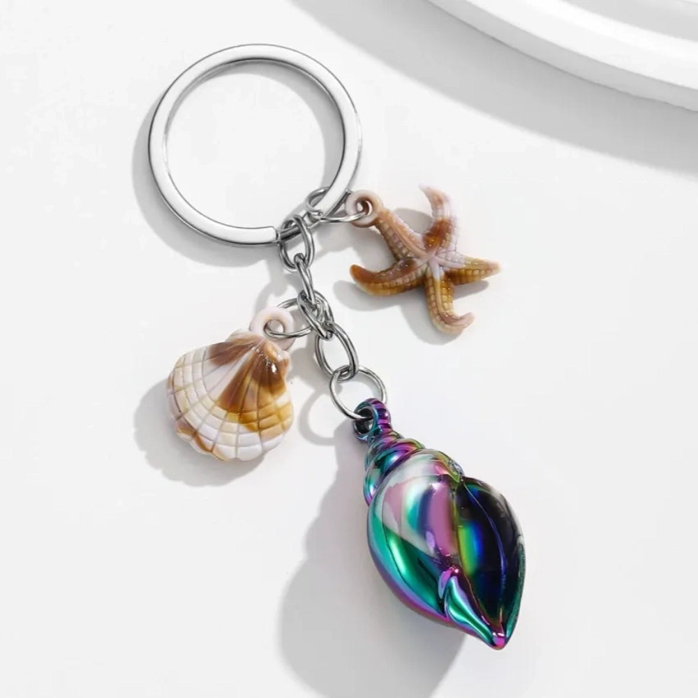8 colorful ocean-themed resin conch shell charm keychains with starfish and scallop shell pendants on silver rings in blue, pink, purple, rainbow, and brown tones. - Black