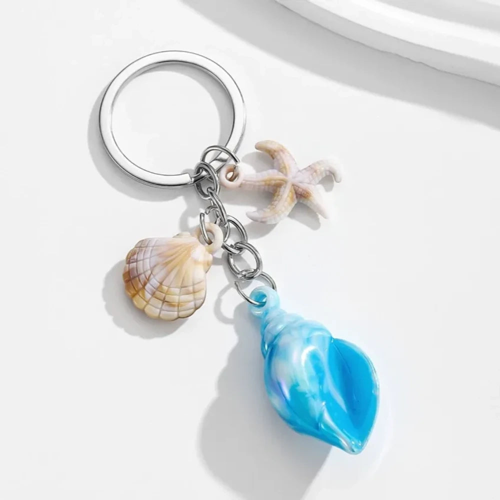 8 colorful ocean-themed resin conch shell charm keychains with starfish and scallop shell pendants on silver rings in blue, pink, purple, rainbow, and brown tones. - Blue