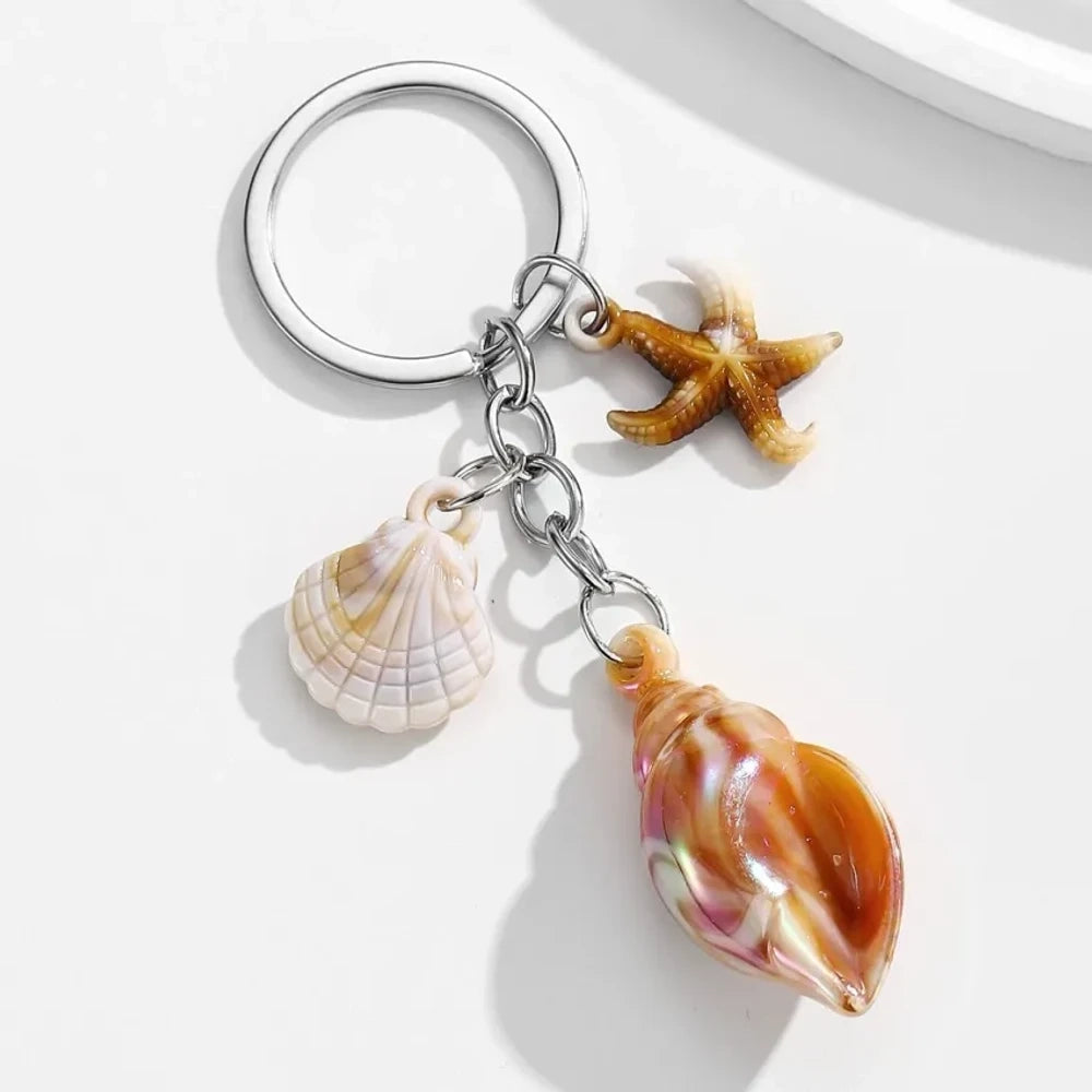 8 colorful ocean-themed resin conch shell charm keychains with starfish and scallop shell pendants on silver rings in blue, pink, purple, rainbow, and brown tones. - Khaki