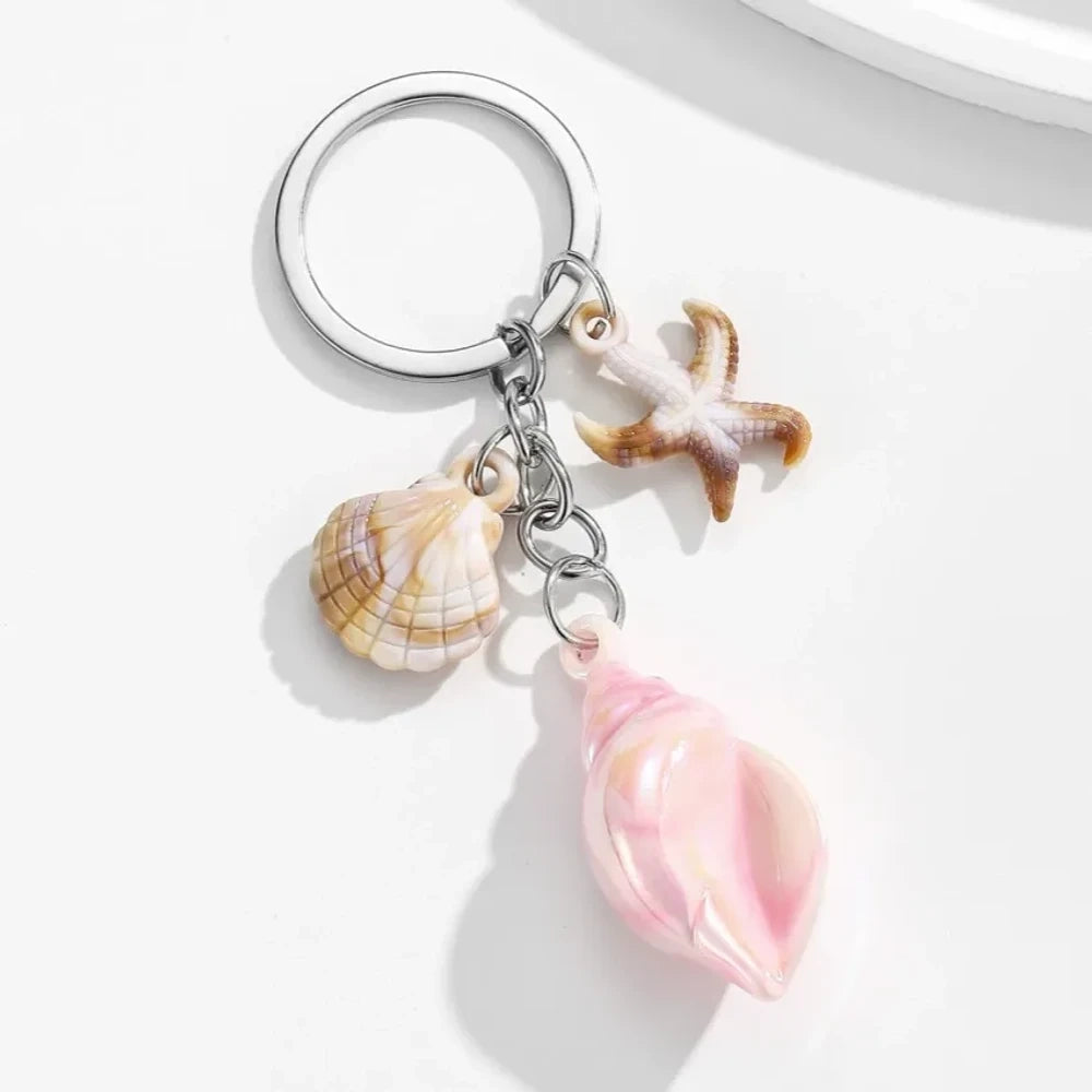 8 colorful ocean-themed resin conch shell charm keychains with starfish and scallop shell pendants on silver rings in blue, pink, purple, rainbow, and brown tones. - Pink
