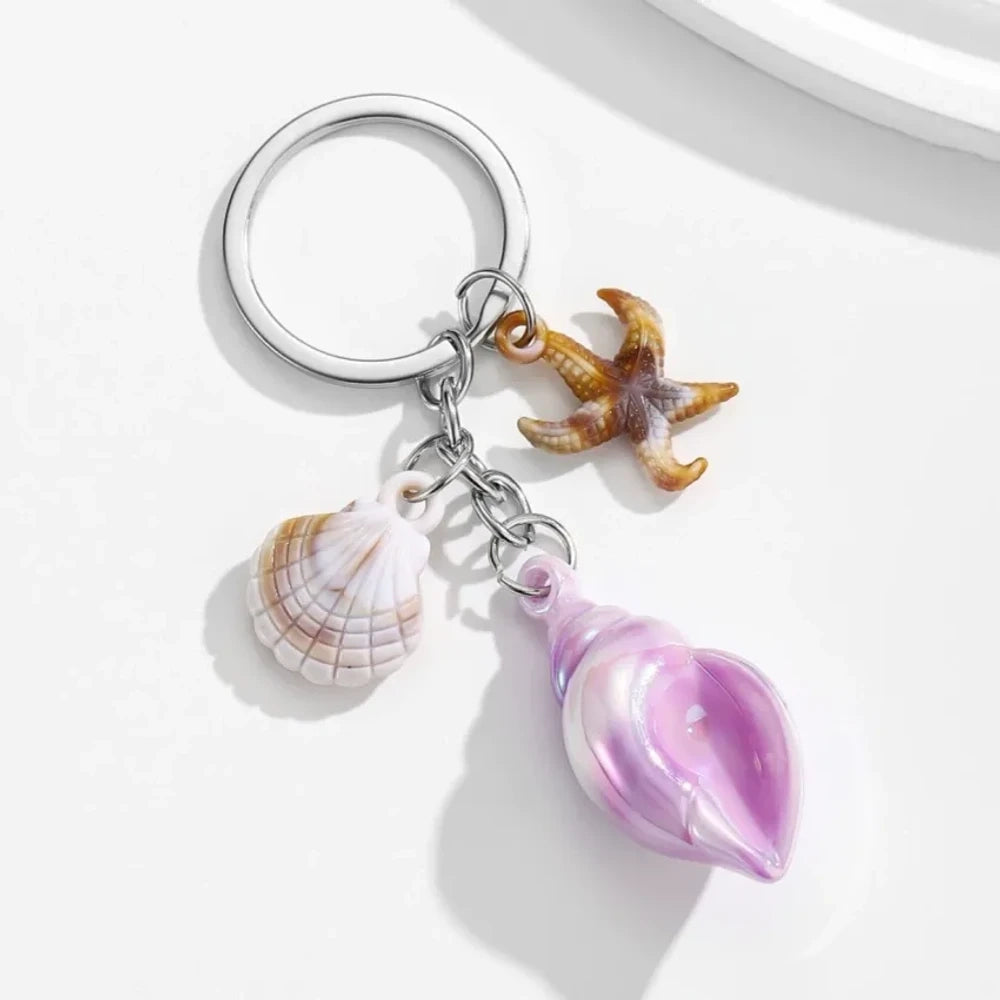 8 colorful ocean-themed resin conch shell charm keychains with starfish and scallop shell pendants on silver rings in blue, pink, purple, rainbow, and brown tones. - Purple
