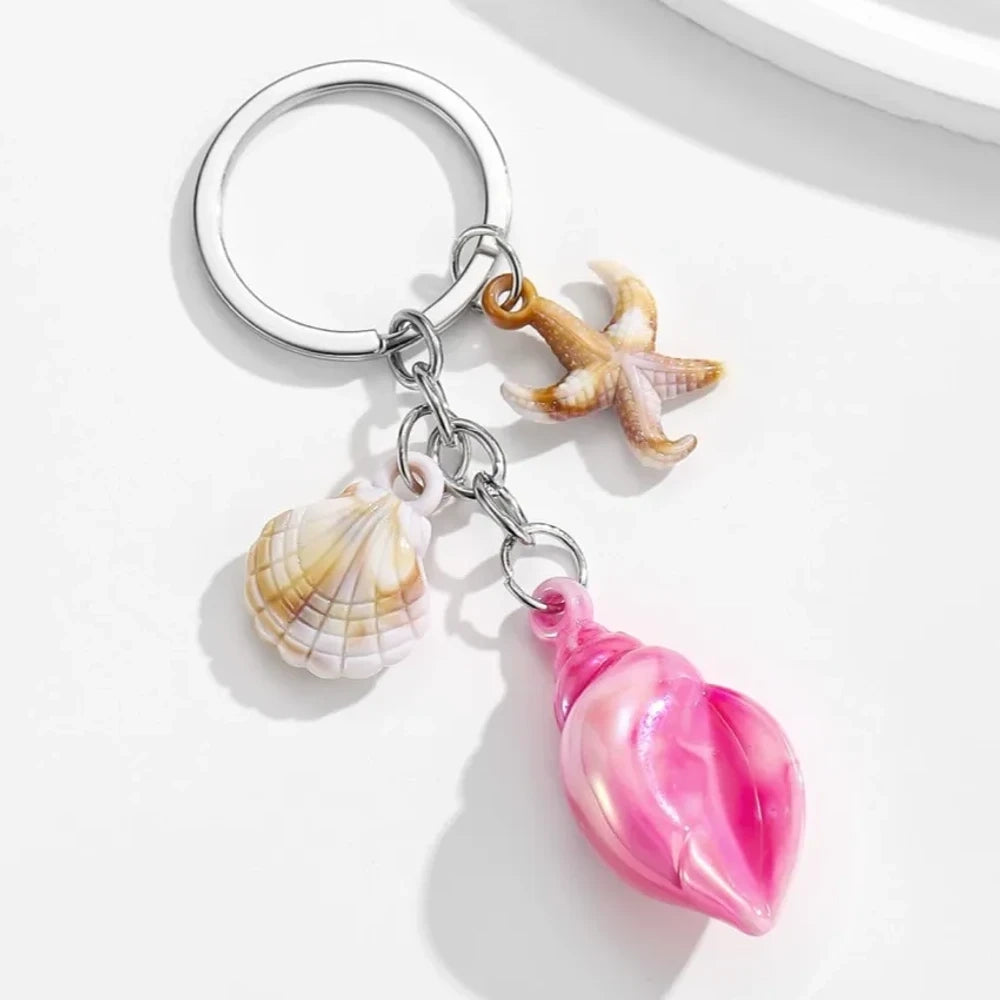 8 colorful ocean-themed resin conch shell charm keychains with starfish and scallop shell pendants on silver rings in blue, pink, purple, rainbow, and brown tones. - Rose Red