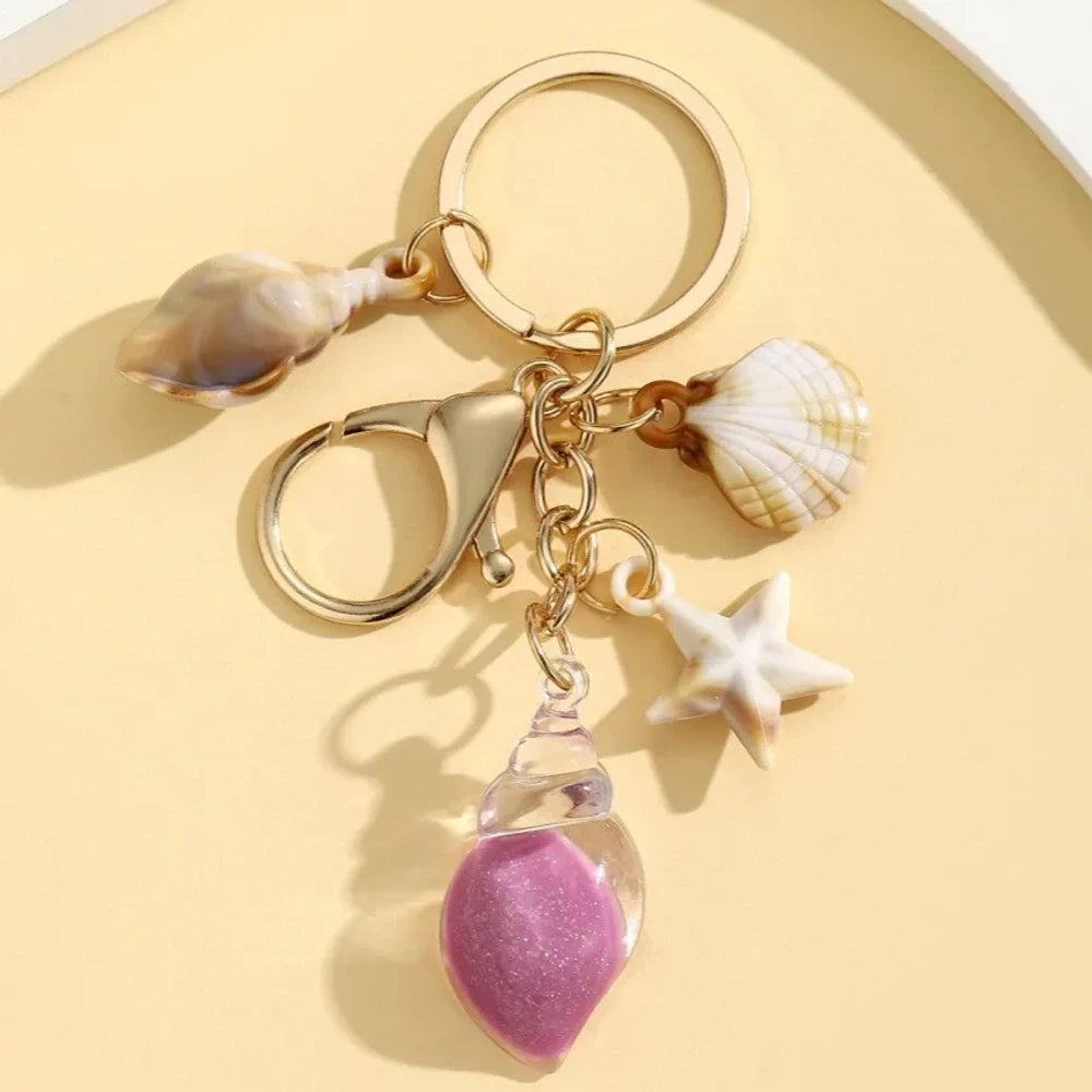 Six ocean-themed keychain charms featuring resin crystal shells in green, purple, blue, clear, and pink, with mini starfish and natural shell accents on gold-tone rings and lobster clasps. - 1
