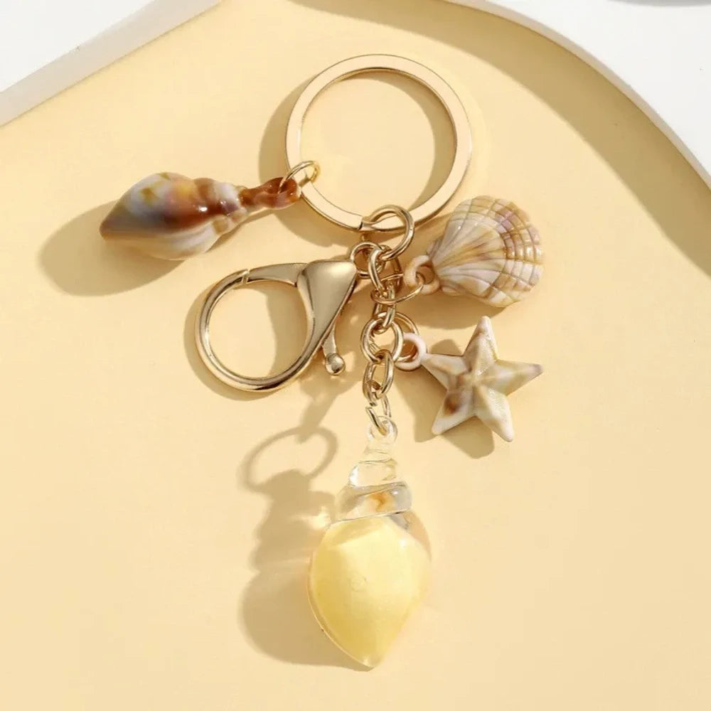 Six ocean-themed keychain charms featuring resin crystal shells in green, purple, blue, clear, and pink, with mini starfish and natural shell accents on gold-tone rings and lobster clasps. - 2