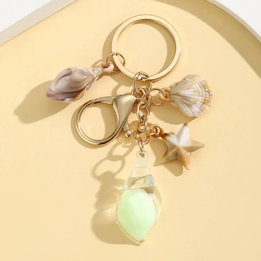 Six ocean-themed keychain charms featuring resin crystal shells in green, purple, blue, clear, and pink, with mini starfish and natural shell accents on gold-tone rings and lobster clasps. - 4