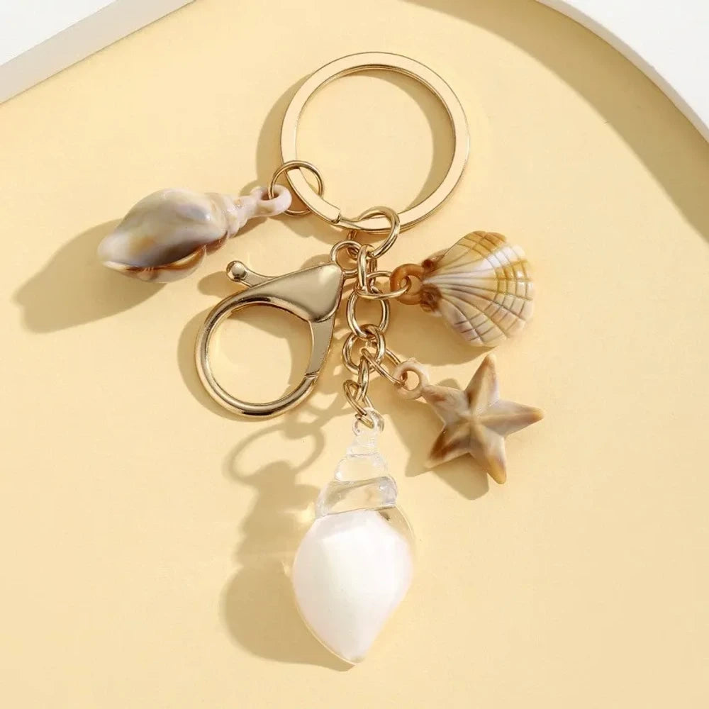 Six ocean-themed keychain charms featuring resin crystal shells in green, purple, blue, clear, and pink, with mini starfish and natural shell accents on gold-tone rings and lobster clasps. - 5