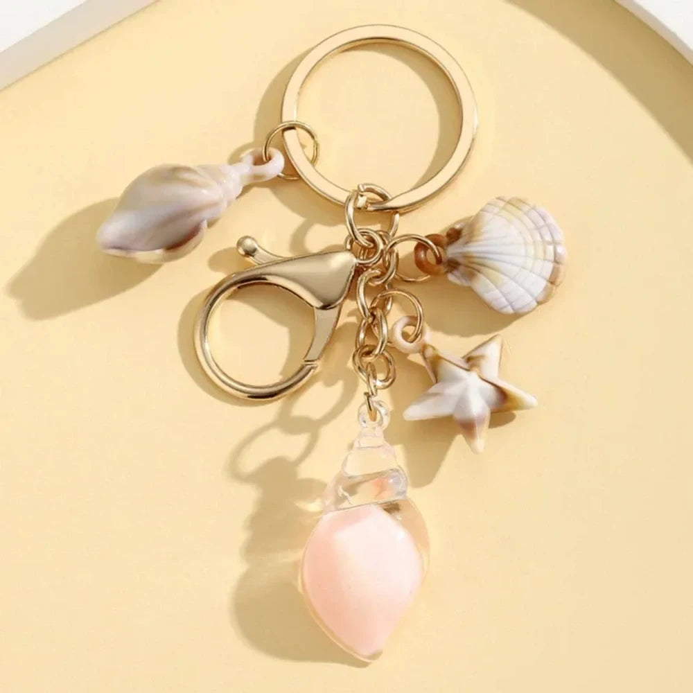 Six ocean-themed keychain charms featuring resin crystal shells in green, purple, blue, clear, and pink, with mini starfish and natural shell accents on gold-tone rings and lobster clasps. - 8