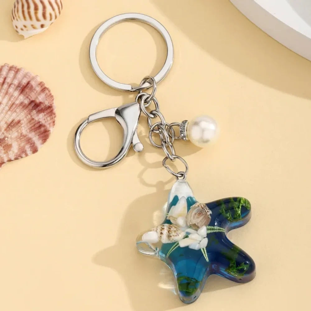 Four ocean starfish-shaped resin keychain charms in blue, pink, light blue, and purple with embedded starfish, flowers, and seaweed, each with a pearl accent and silver lobster clasp ring. - Dark Blue