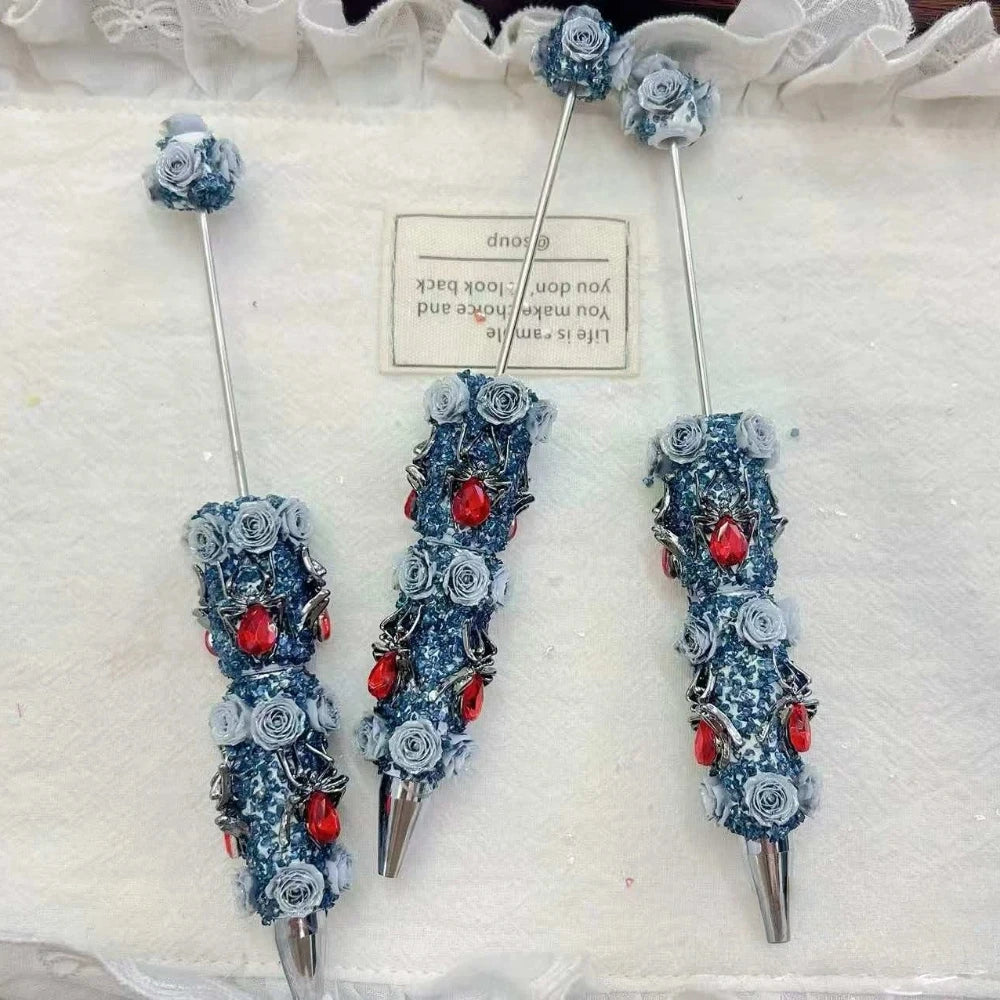 Blue rose gothic rhinestone pens with silver detailing and red teardrop gem accents on a white background