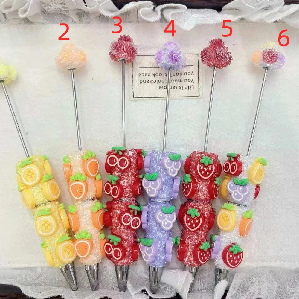 Assorted fruit glitter rhinestone pens with fluffy pompom tops, including lemon, orange, cherry, grape, and strawberry designs