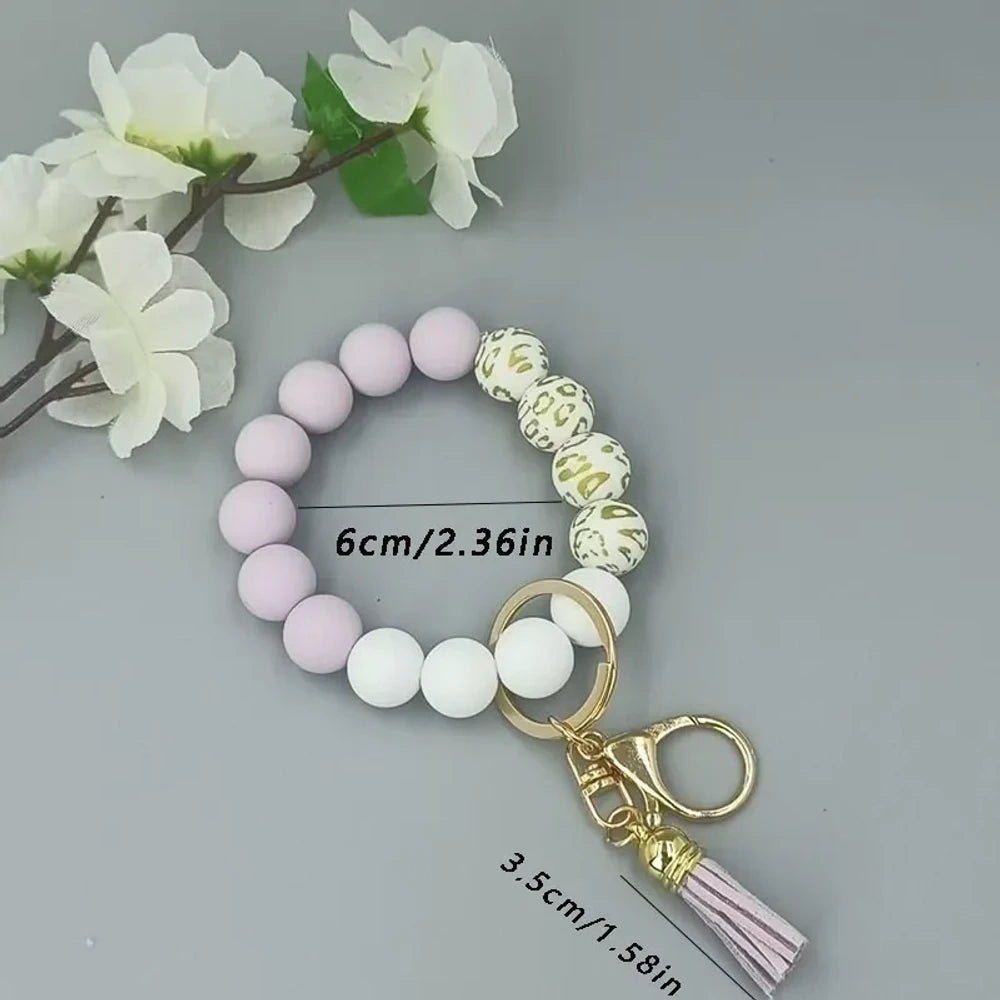 Pastel silicone bead bracelets in peach, lavender, and purple with leopard print beads, gold lobster clasps, and tassel charms on a gray background. - Purple