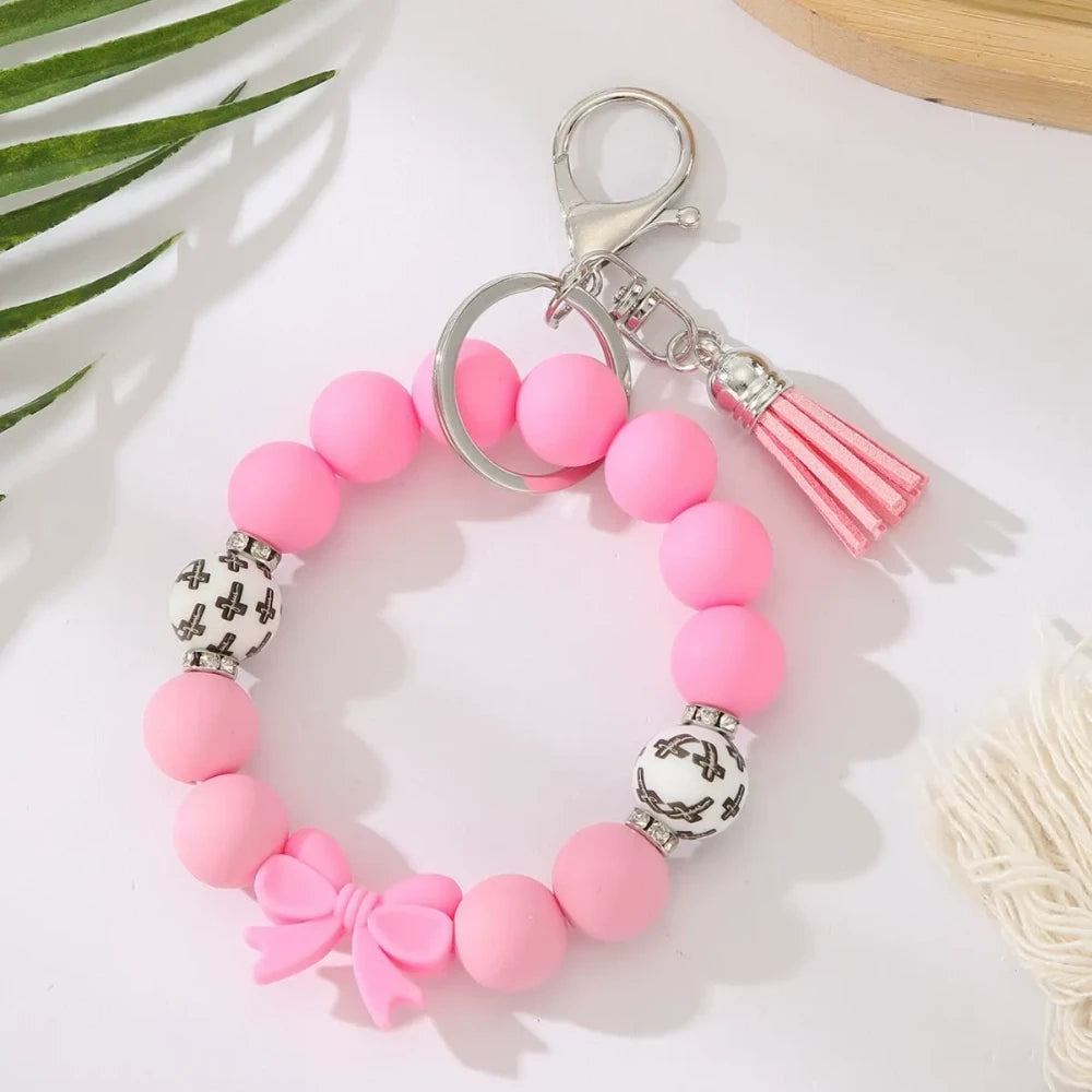 Seven colorful pastel solid silicone bead bracelet keychains in teal, purple, black multicolor, white, pink, and yellow, each featuring bow charms or tassels and silver lobster clasp hardware, arranged on a white surface. - Rose Red
