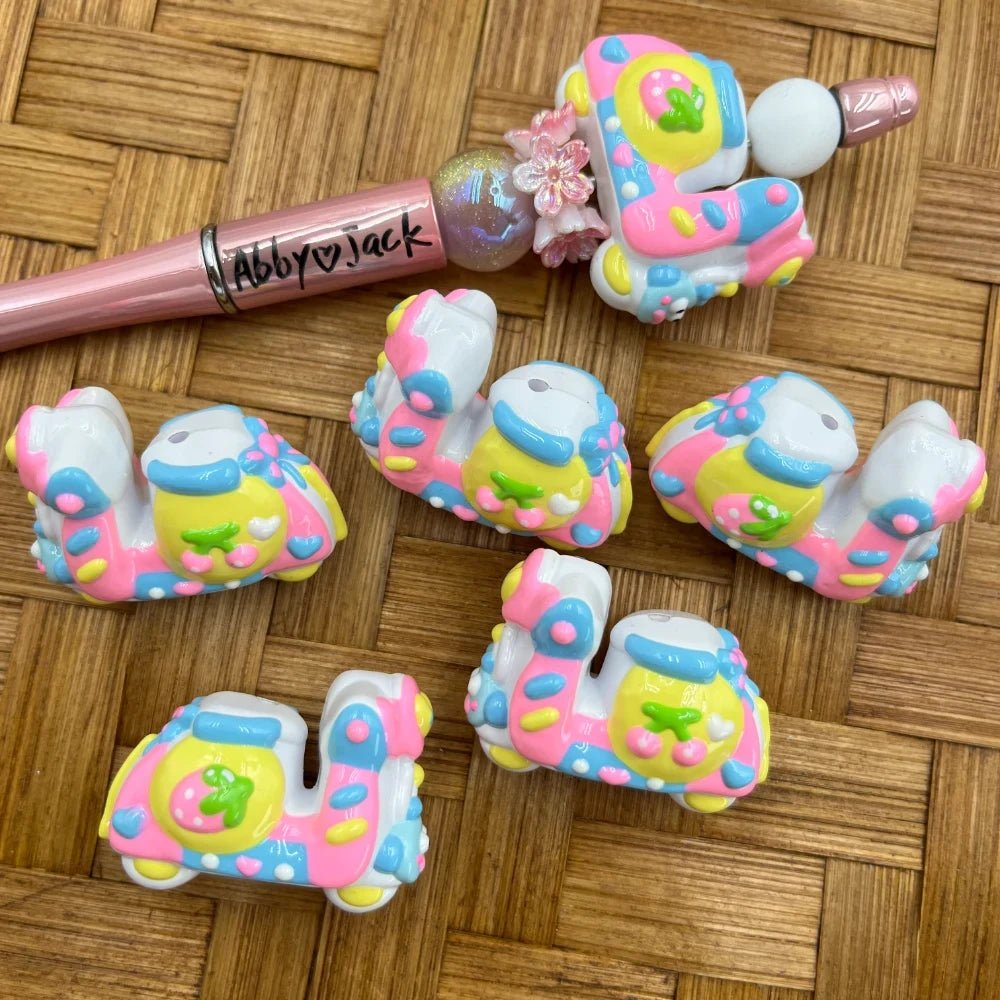 Colorful pastel pink yellow and blue train acrylic beads with floral details displayed next to a decorated beadable pen on a wicker surface
