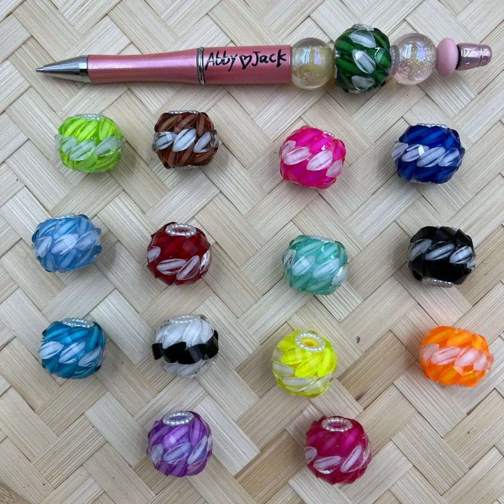 Assorted petal leaf textured acrylic fancy beads in 14 colors including pink, blue, green, orange, purple, black, and yellow, displayed on a woven surface next to a pink beadable pen labeled Abby and Jack.