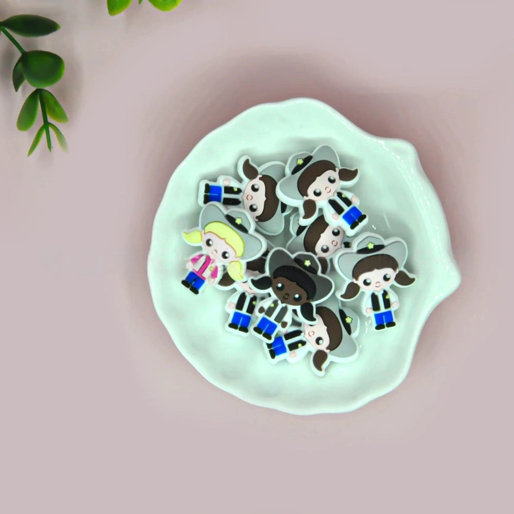 Assorted police girl silicone focal beads in multiple skin tones displayed on a white ceramic dish, featuring cute cartoon cop characters in blue uniforms with stars, perfect for beadable pens, keychains, and badge reels.
