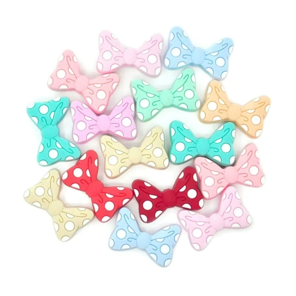 Assorted pastel and bold color polka dot bow silicone focal beads with white dots, arranged in a circle on a white background, for DIY jewelry making and beadable pens.