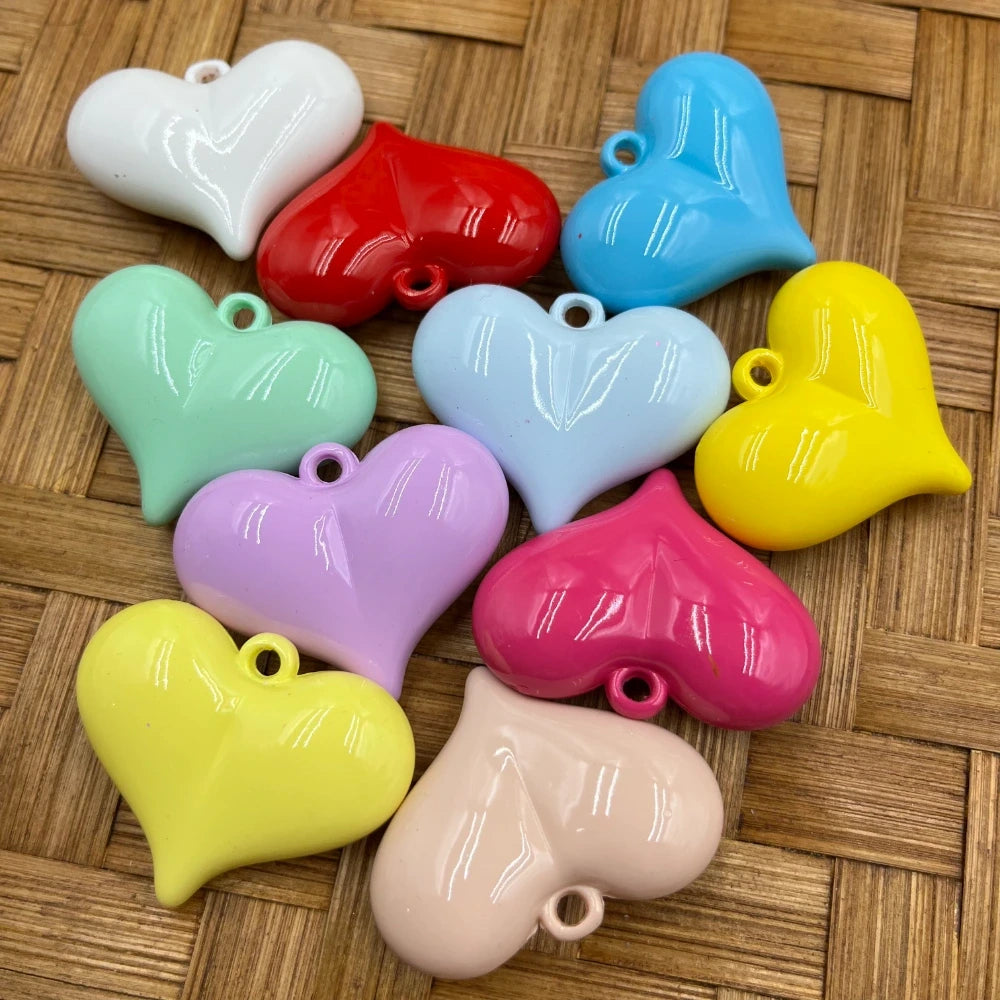 Ten glossy puffy heart-shaped acrylic bead charms in assorted colors including white, red, mint, lavender, yellow, light blue, baby pink, hot pink, beige, and sky blue, displayed on a woven surface.