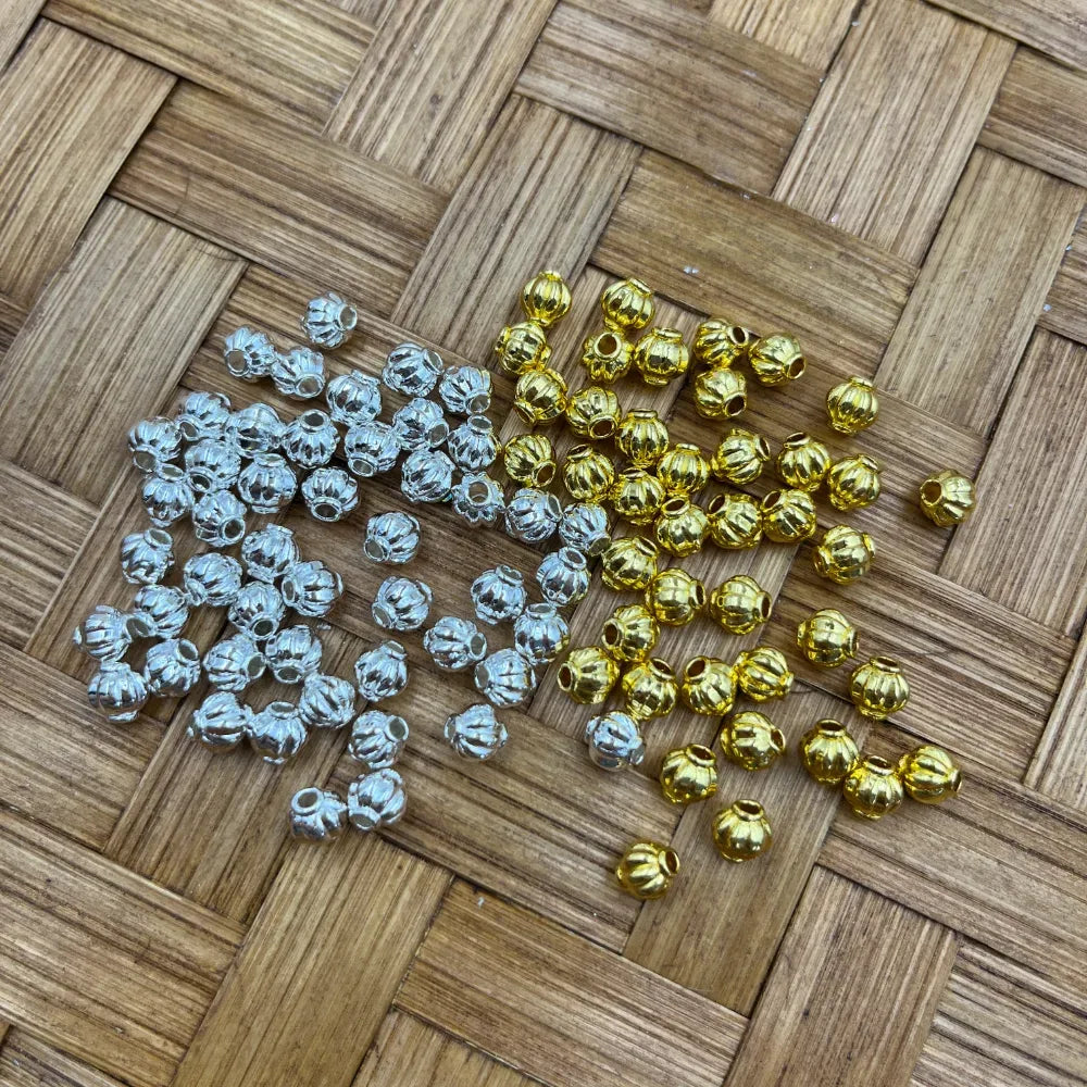 Gold and silver pumpkin-shaped ridged metal spacer beads arranged on a woven bamboo mat, suitable for beadable pens, keychains, bracelets, and DIY jewelry making.