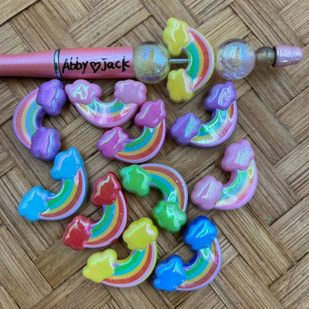 Colorful acrylic rainbow cloud beads in pastel and bright colors with iridescent shimmer finish, shown with a beadable pen on a woven surface