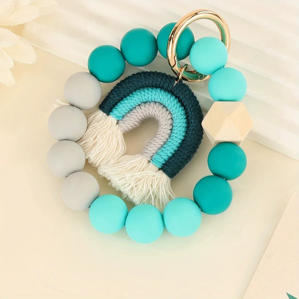 Three rainbow macrame wristlet keychains with colorful silicone beads in red, teal, and pastel color combinations on a cream background. - Blue