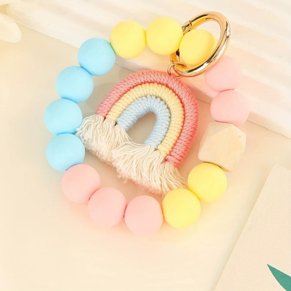 Three rainbow macrame wristlet keychains with colorful silicone beads in red, teal, and pastel color combinations on a cream background. - Pink