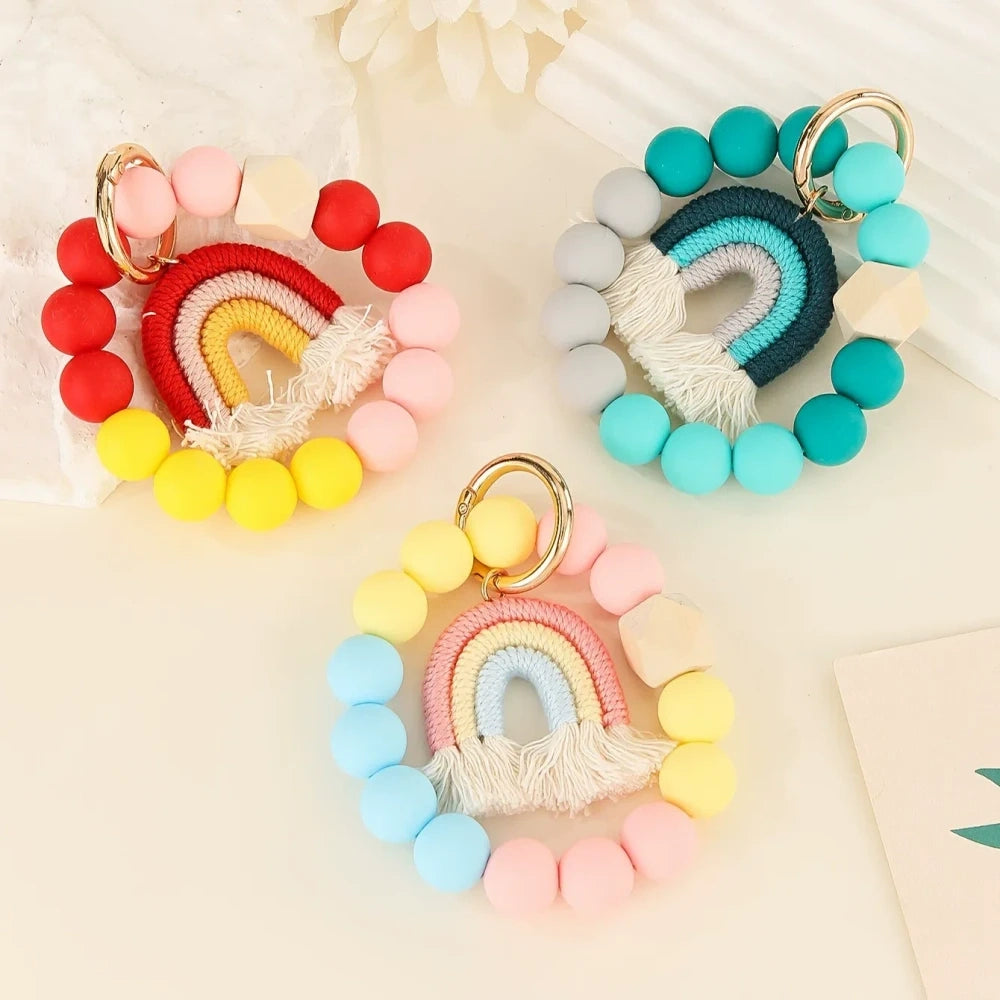 Three rainbow macrame wristlet keychains with colorful silicone beads in red, teal, and pastel color combinations on a cream background. - Random Mixed