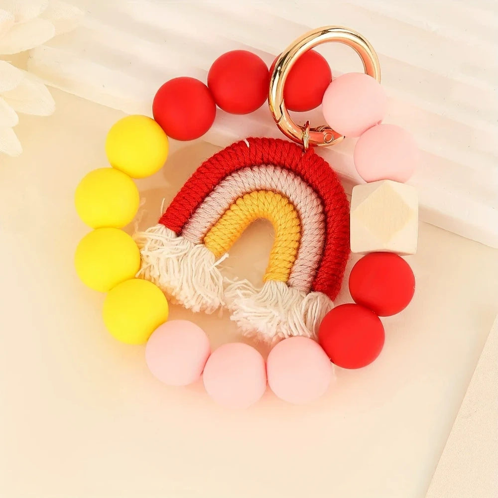 Three rainbow macrame wristlet keychains with colorful silicone beads in red, teal, and pastel color combinations on a cream background. - Red
