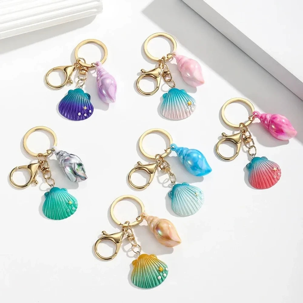Six colorful resin ocean shell and conch keychain charms in purple, teal, pink, blue, and gradient colors with gold lobster clasp hardware on white background
