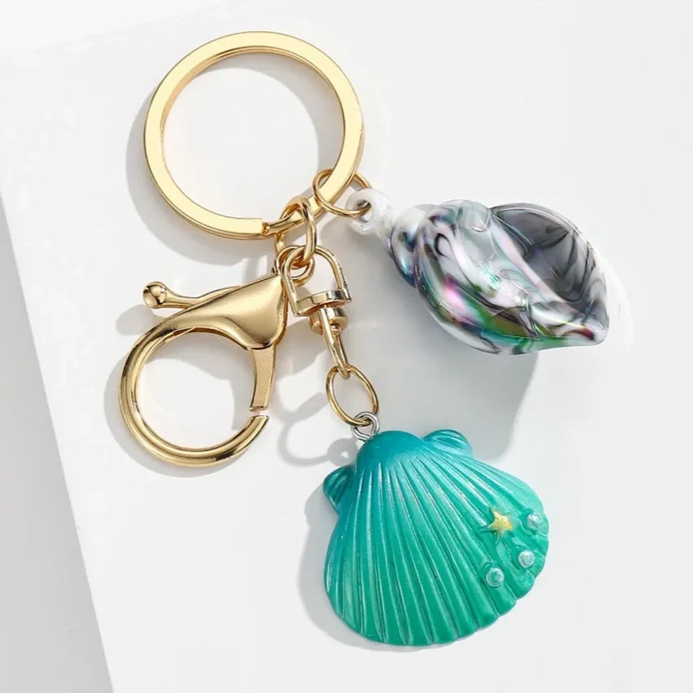 Six colorful resin ocean shell and conch keychain charms in purple, teal, pink, blue, and gradient colors with gold lobster clasp hardware on white background - 1