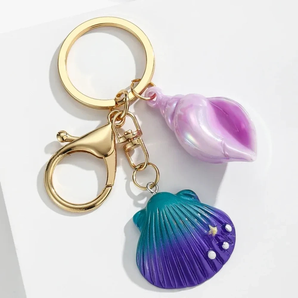 Six colorful resin ocean shell and conch keychain charms in purple, teal, pink, blue, and gradient colors with gold lobster clasp hardware on white background - 2