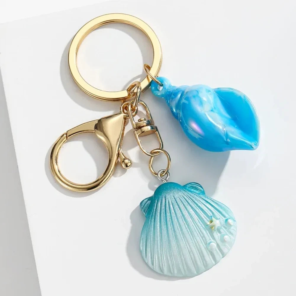 Six colorful resin ocean shell and conch keychain charms in purple, teal, pink, blue, and gradient colors with gold lobster clasp hardware on white background - 3