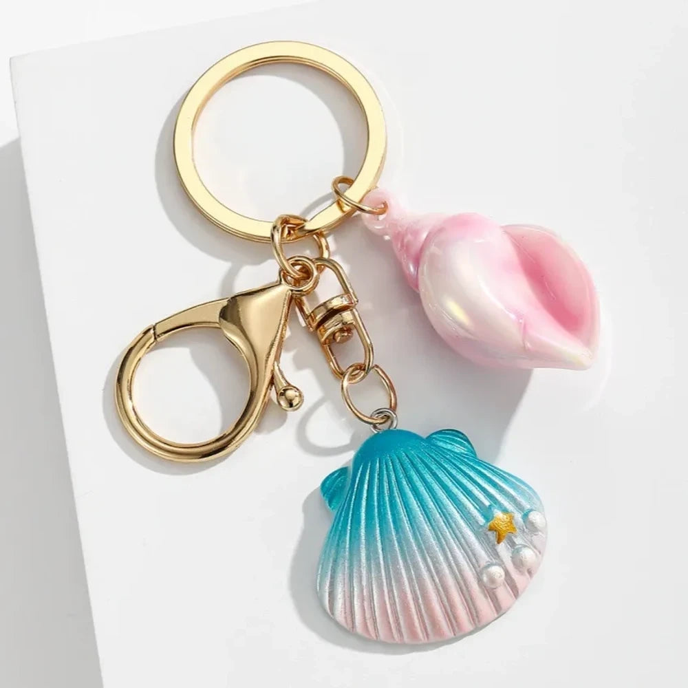 Six colorful resin ocean shell and conch keychain charms in purple, teal, pink, blue, and gradient colors with gold lobster clasp hardware on white background - 4