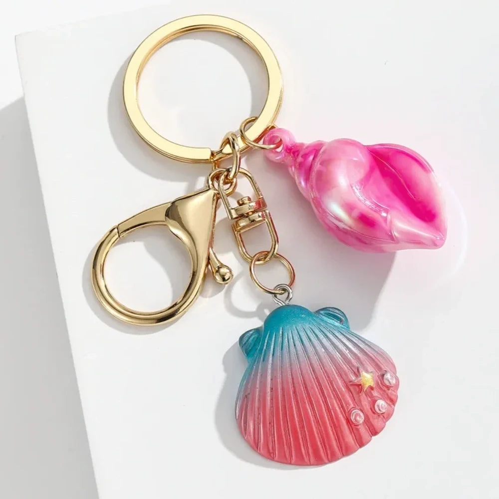 Six colorful resin ocean shell and conch keychain charms in purple, teal, pink, blue, and gradient colors with gold lobster clasp hardware on white background - 5