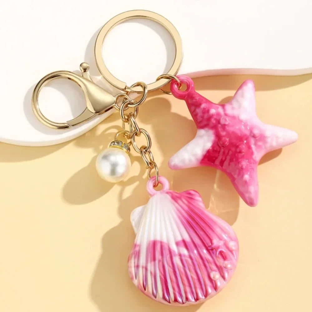 Six colorful resin ocean shell and starfish keychain charms with pearl beads in pink, white, purple, blue, iridescent, and hot pink, displayed on a yellow background. - 1