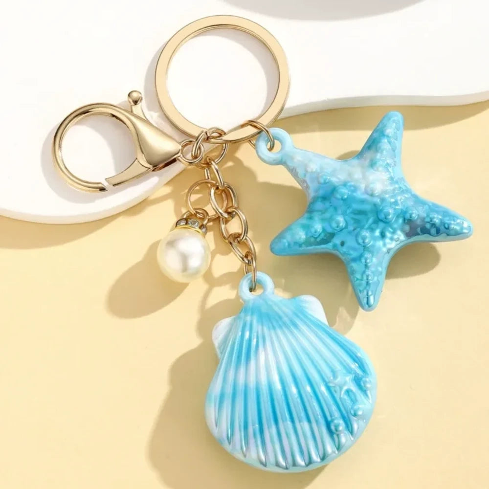 Six colorful resin ocean shell and starfish keychain charms with pearl beads in pink, white, purple, blue, iridescent, and hot pink, displayed on a yellow background. - 5