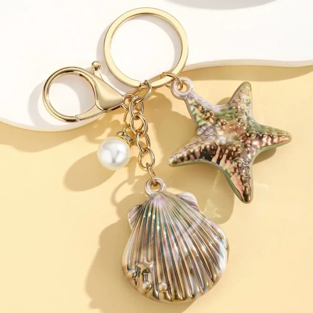 Six colorful resin ocean shell and starfish keychain charms with pearl beads in pink, white, purple, blue, iridescent, and hot pink, displayed on a yellow background. - 6
