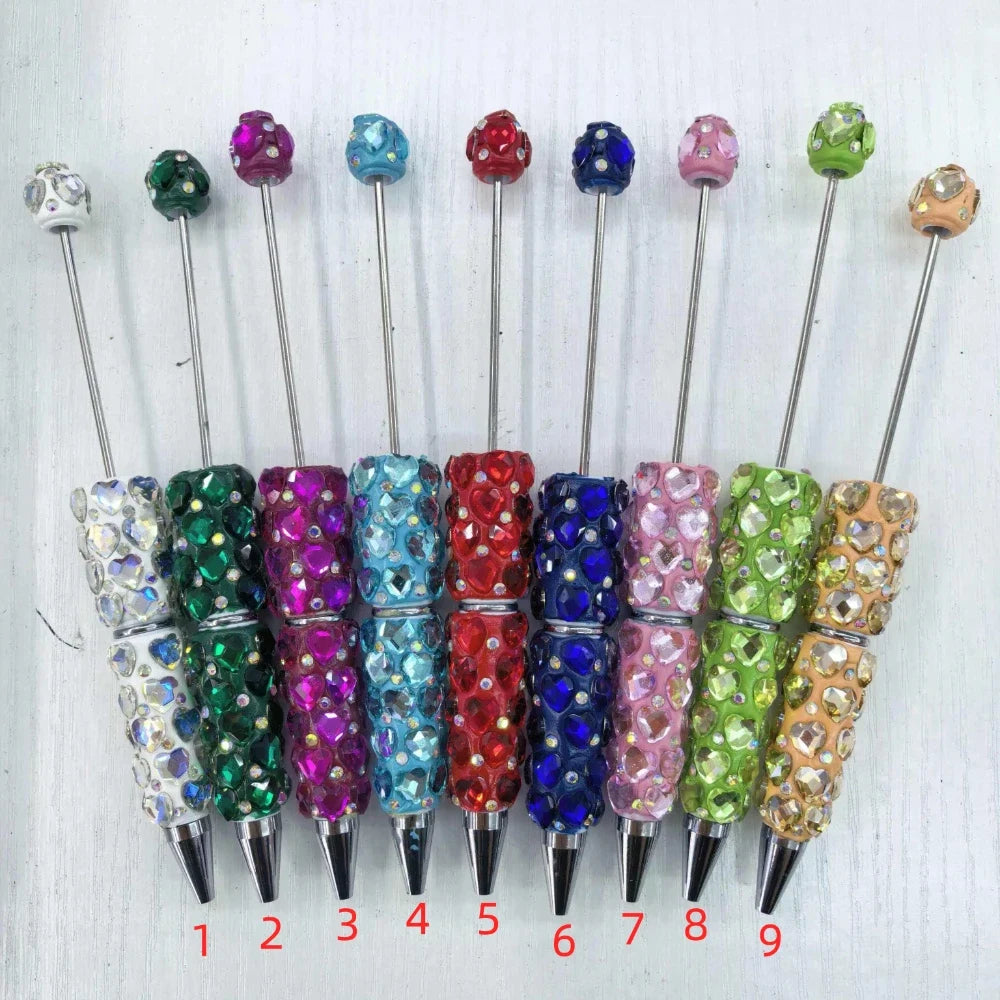 9 rhinestone studded beadable pens in assorted colors including white, green, purple, teal, red, blue, pink, light green, and gold, each with a matching rhinestone bead topper and silver metal tip, numbered 1 through 9.