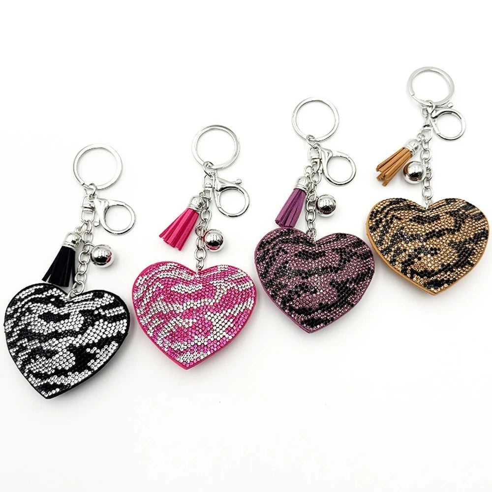 Four rhinestone-covered heart-shaped keychain charms in black, pink, purple, and gold leopard/zebra animal print patterns with tassel and silver ball accents on metal key rings.